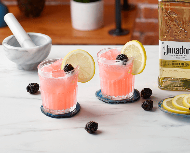 el Jimador Bramble cocktail on a table with a blackberries and el Jimador Reposado bottle.