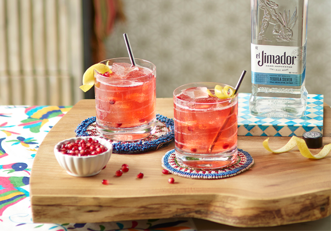 el Jimador Brisa cocktails on a table with a lemon twists, pomegranate seeds and el Jimador Silver bottle.