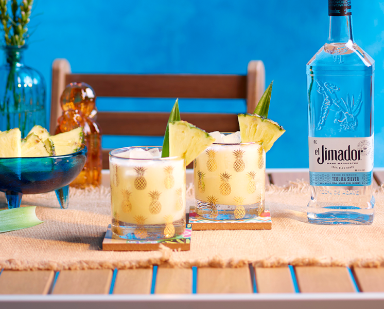 el Jimador Pina Coconut Margarita cocktails on a table with a pineapple slices and el Jimador Silver bottle.