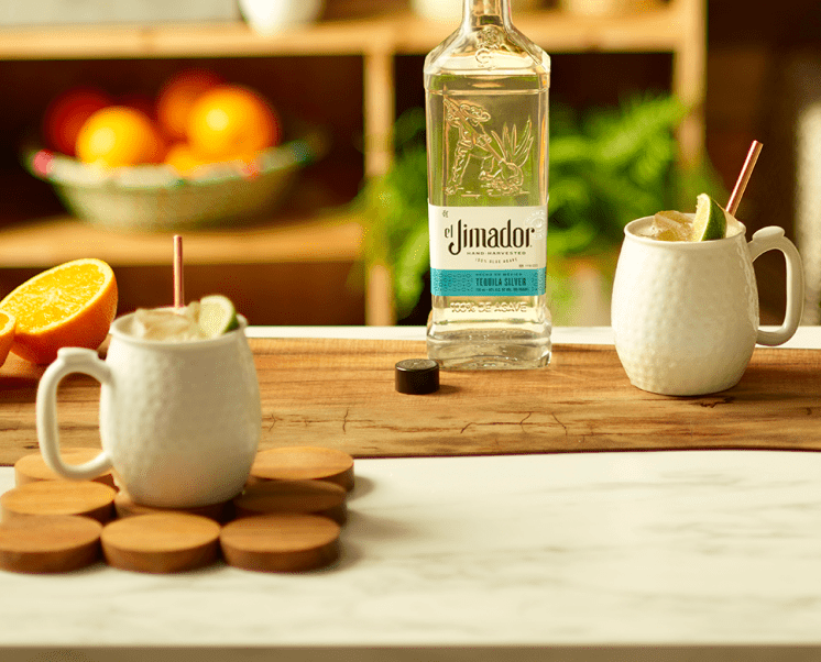 el Jimador Tequila Mule cocktails on a table with orange slices and el Jimador Silver bottle.