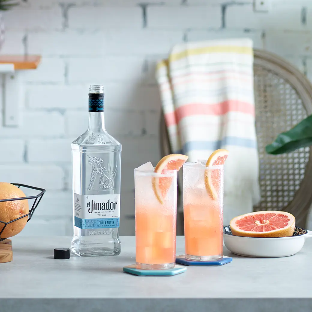 An image of two cocktails on a counter with a bottle of el Jimador Silver tequila and a sliced grapefruit
