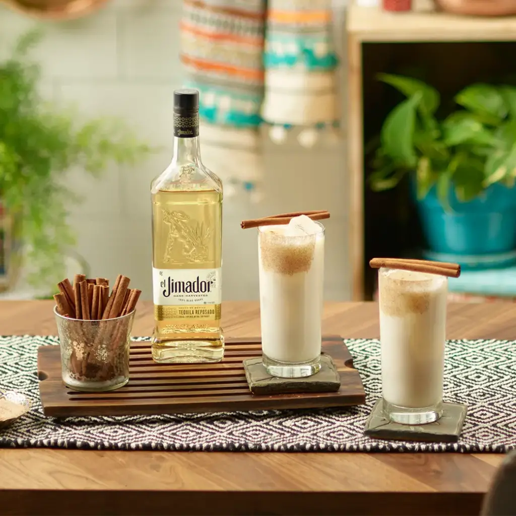 An image of two cocktails on a table with a bottle of el Jimador Reposado tequila and a cup of cinnamon sticks