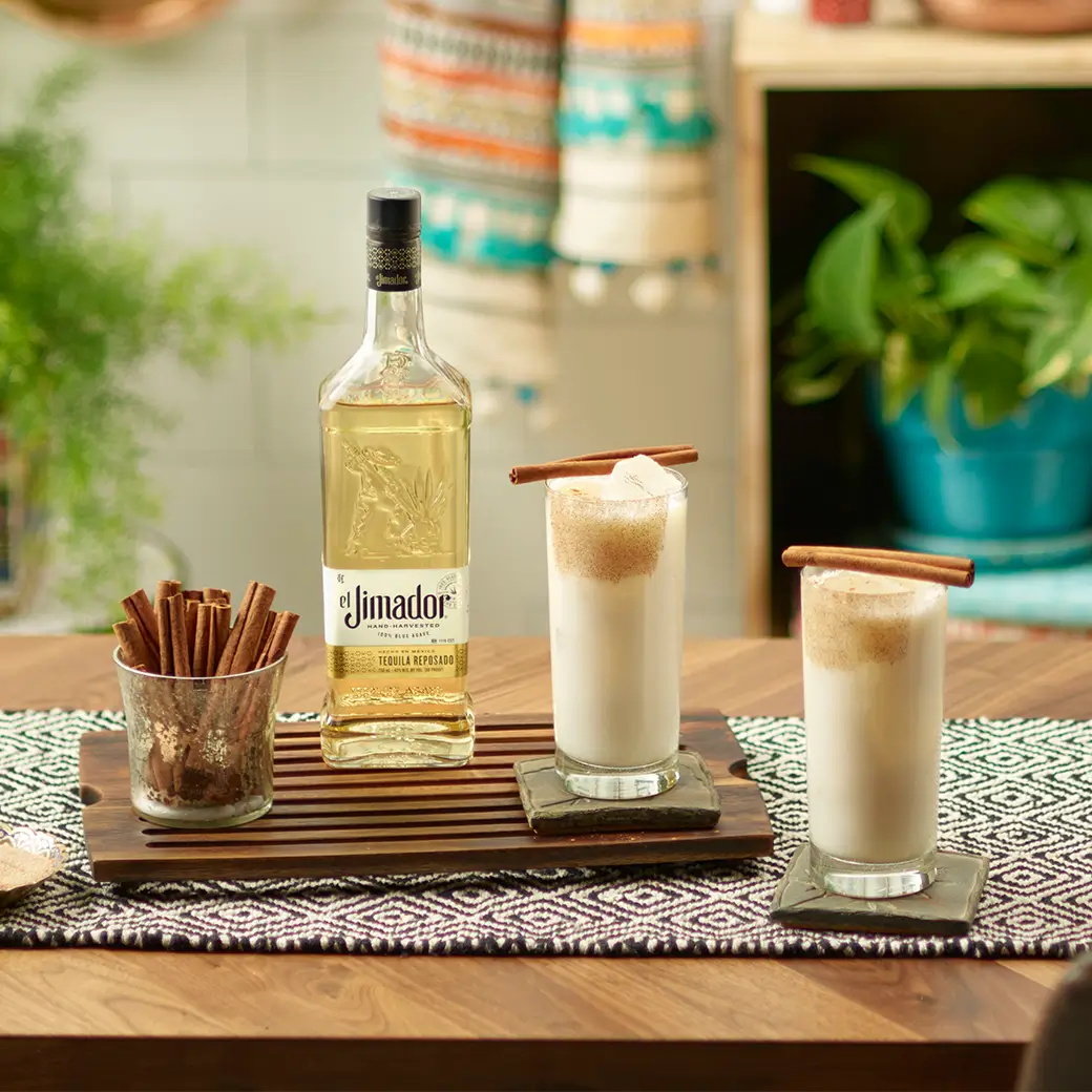 An image of two cocktails on a table with a bottle of el Jimador Reposado tequila and a cup of cinnamon sticks