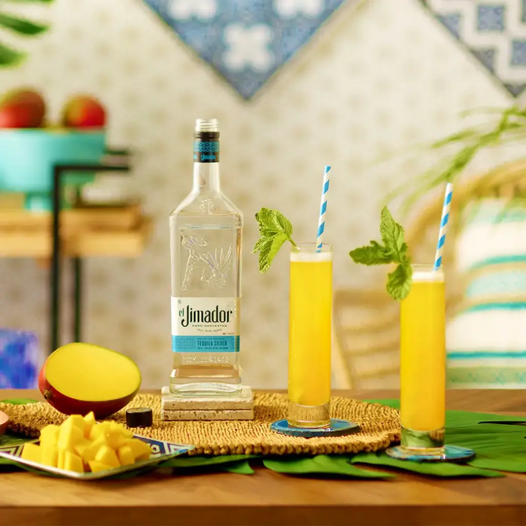 An image of two cocktails on a counter with a bottle of el jimador Silver tequila and sliced mango