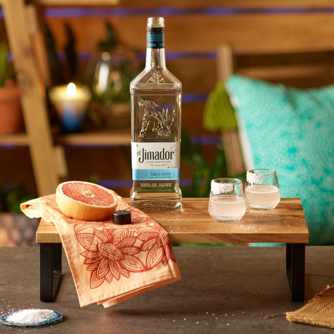 An image of two cocktails on a wooden tray with a bottle of el Jimador Silver tequila, a small peach colored napkin, and a sliced grapefruit
