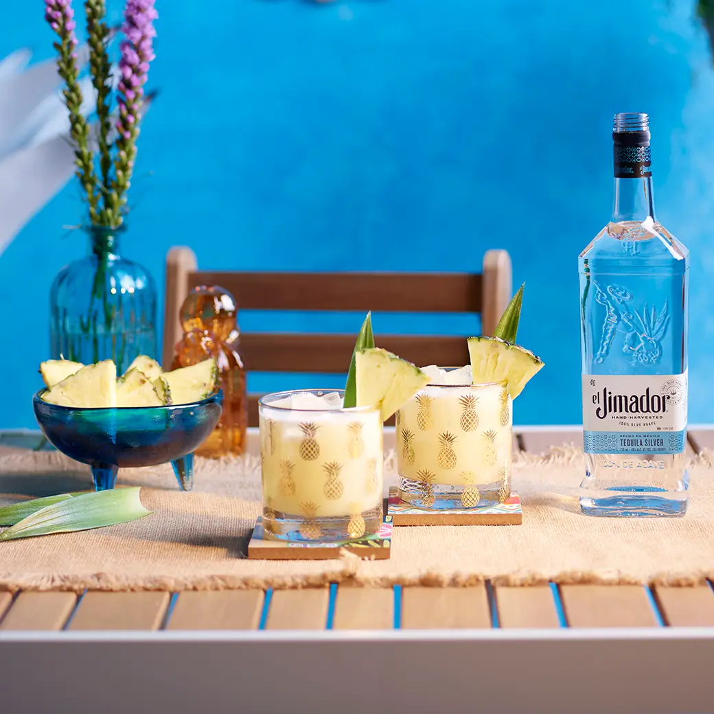 An image of two margaritas on a table with a bottle of el Jimador Silver tequila and a bowl of sliced pineapple