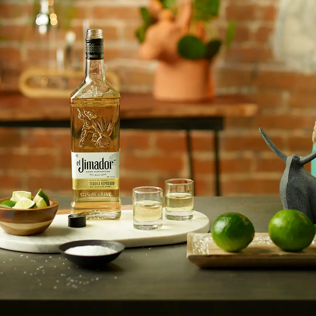 An image of two shots on a tray along with a bottle of el Jimador Reposado tequila, a bowl of salt, and a bowl of sliced limes