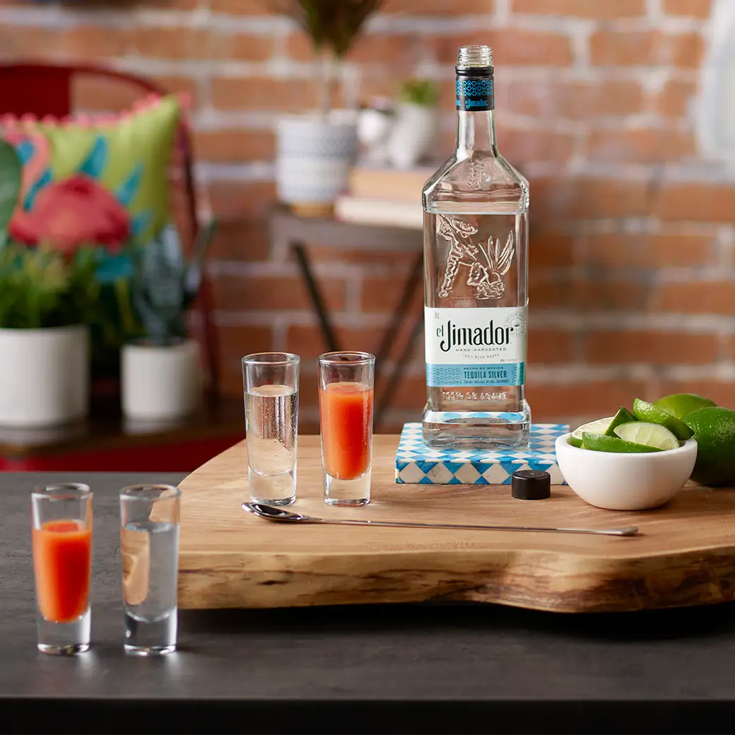 An image of four Sangrita shots on a counter with lime wedges and a bottle of el Jimador Silver tequila